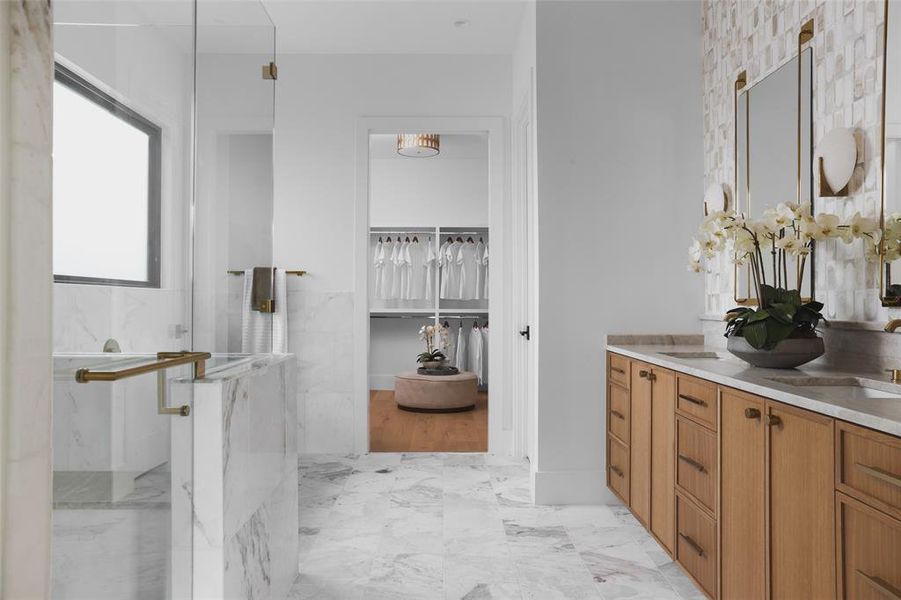 A marble-clad bath features intricate mosaic tile, a walk-in shower with two showerheads and a soaking tub set under a bright frosted window.