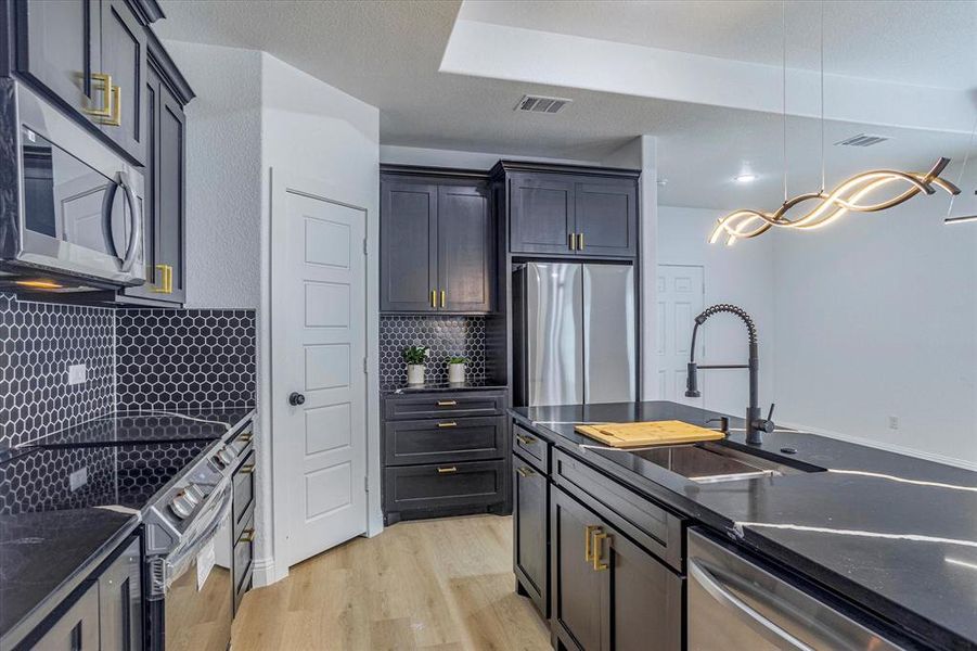 Kitchen featuring light wood-type flooring, appliances with stainless steel finishes, decorative light fixtures, backsplash, and sink
