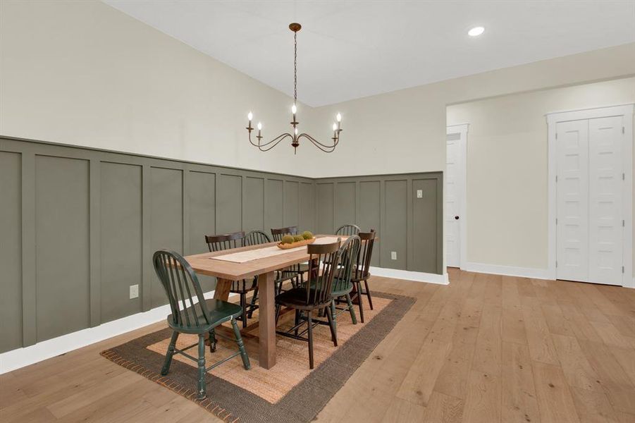 The elegant dining room is open to the family and kitchen area.  The room is accented with a stylish chandelier and includes a sophisticated wainscoting wall treatment in a calming khaki green tone. Natural hardwood floors add warmth to the space, and there are two white doors to the right offer access to a beautiful pantry.