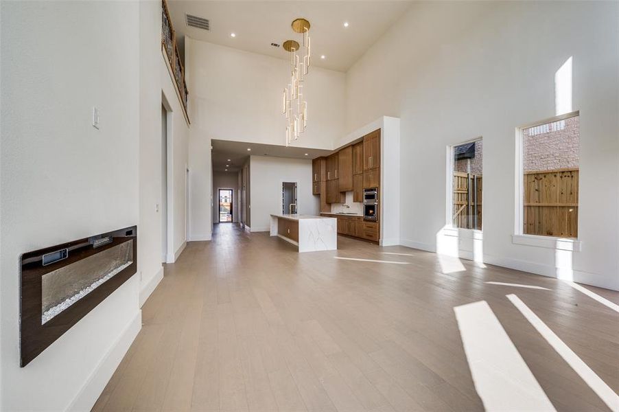 Unfurnished living room with an inviting chandelier, light hardwood / wood-style flooring, and a high ceiling