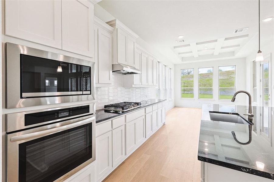 Kitchen with wall chimney range hood, coffered ceiling, backsplash, light wood-type flooring, and sink