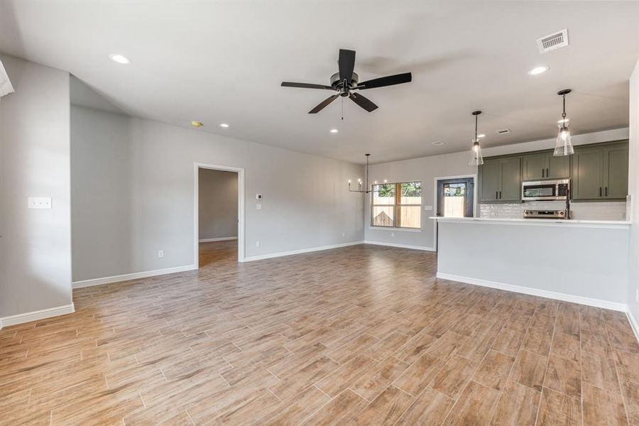 Unfurnished living room featuring ceiling fan with notable chandelier and light hardwood / wood-style floors