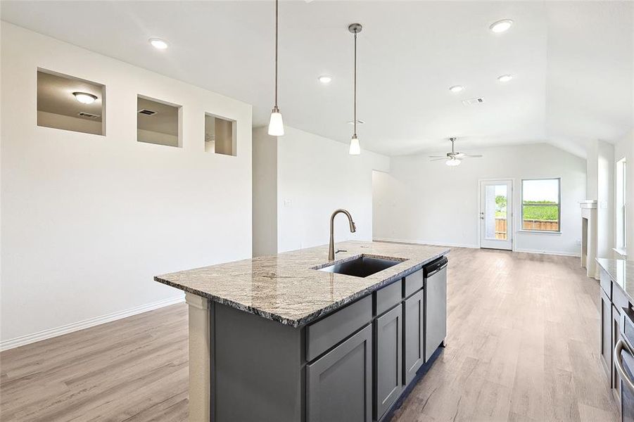 Kitchen with light wood-type flooring, light stone counters, sink, an island with sink, and ceiling fan