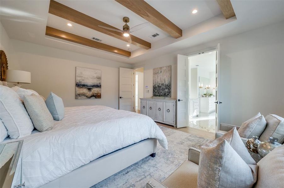 Bedroom with beamed ceiling, ceiling fan, a tray ceiling, light hardwood / wood-style flooring, and ensuite bath