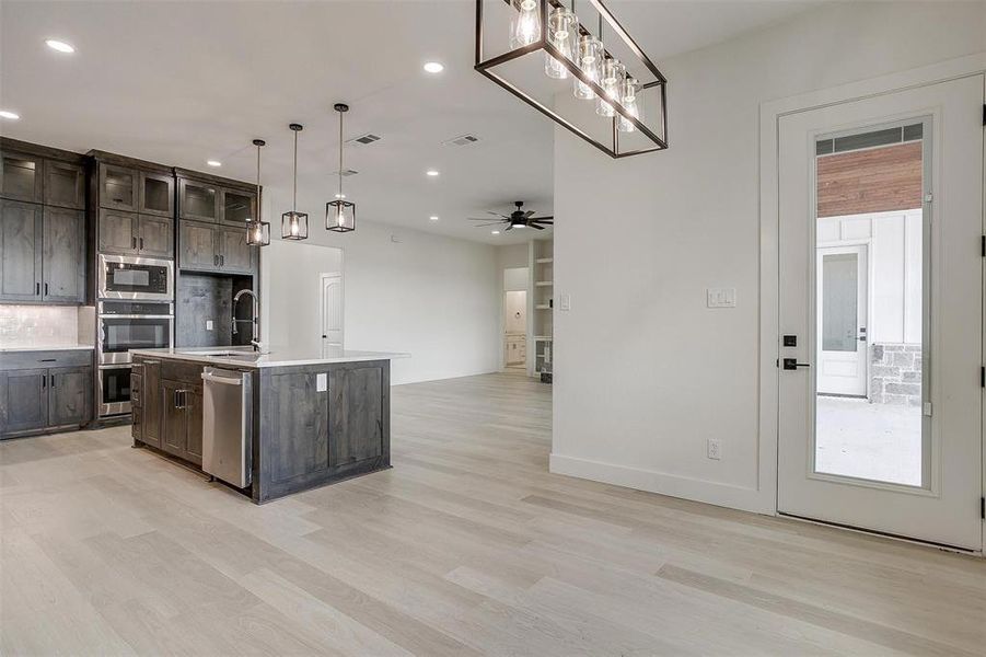 Kitchen with pendant lighting, appliances with stainless steel finishes, an island with sink, ceiling fan, and light wood-type flooring