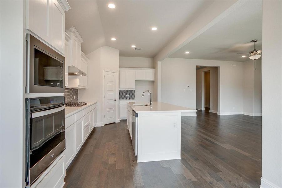 Kitchen featuring dark hardwood / wood-style floors, ventilation hood, an island with sink, white cabinets, and decorative backsplash