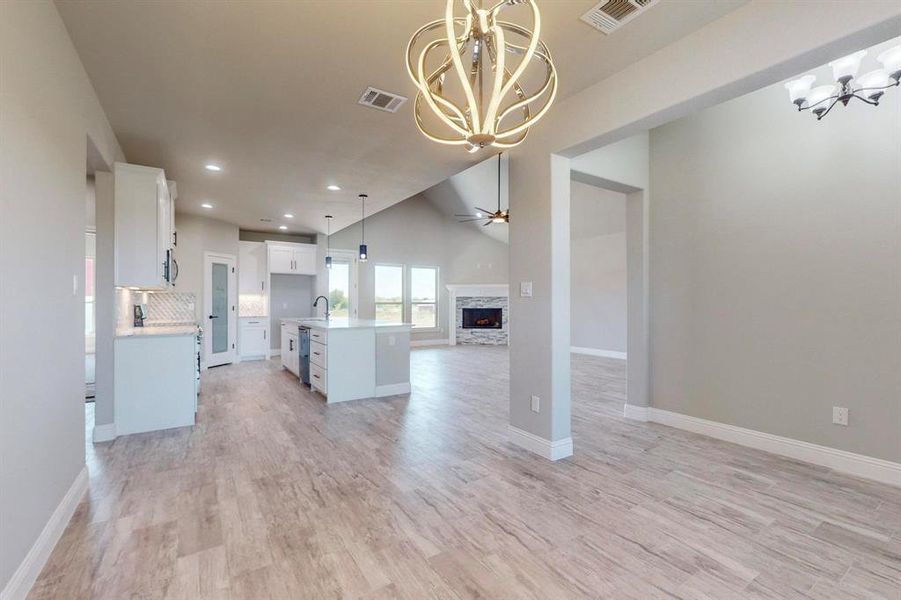 Kitchen featuring light hardwood / wood-style floors, white cabinetry, an island with sink, ceiling fan with notable chandelier, and a stone fireplace