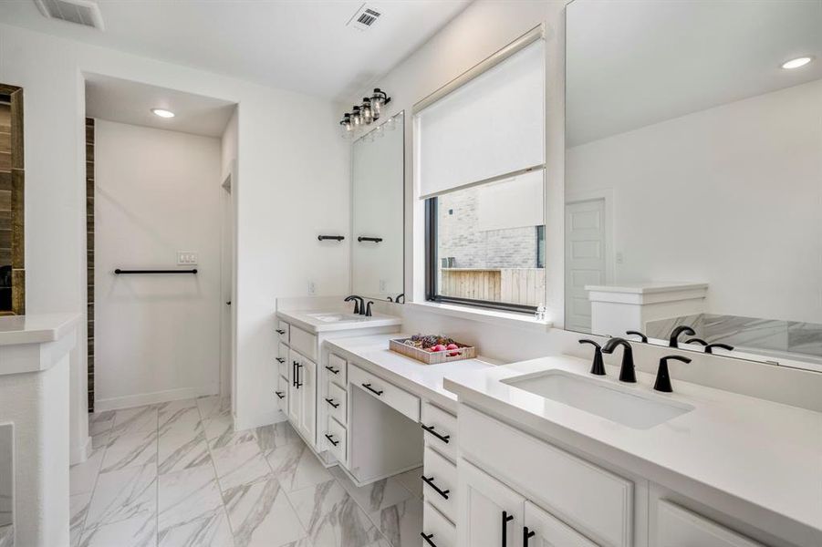 You'll love getting ready in this light and bright primary bathroom! The primary bathroom includes a large vanity with dual sinks, make-up space, quartz counters, black plumbing fixtures, and white cabinets.