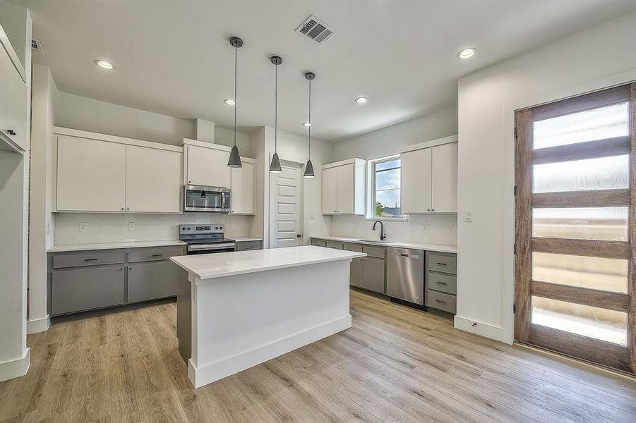 Kitchen featuring gray cabinets, white cabinets, appliances with stainless steel finishes, and a kitchen island