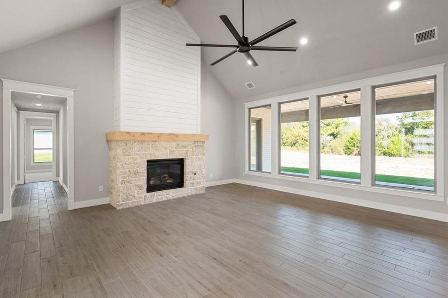 Unfurnished living room featuring ceiling fan, high vaulted ceiling, a fireplace, and hardwood / wood-style floors