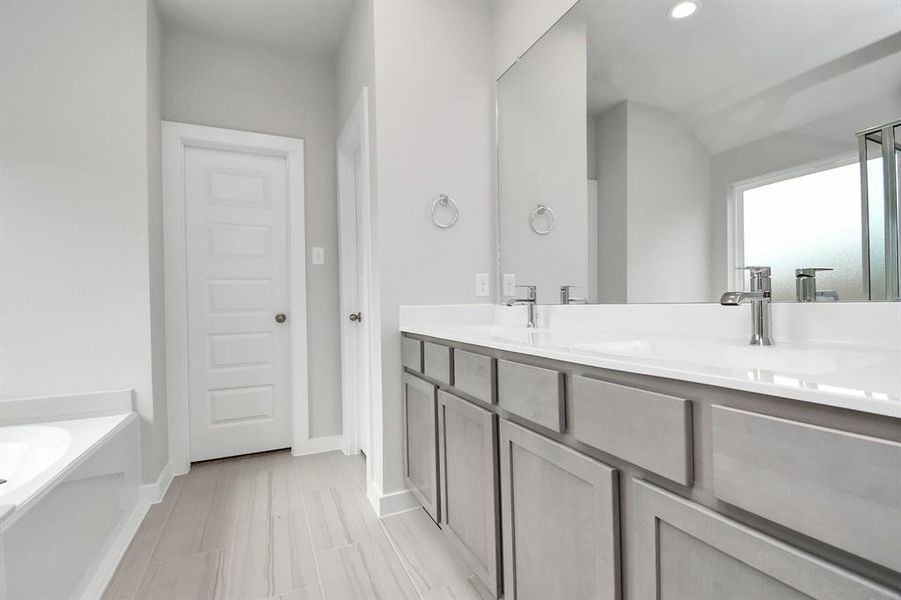 Elevate your daily routine at the elegant vanity, now equipped with double sinks, light countertops, modern hardware, and bright recessed lights. Sample photo of completed home with similar plan. Actual color and selections may vary.