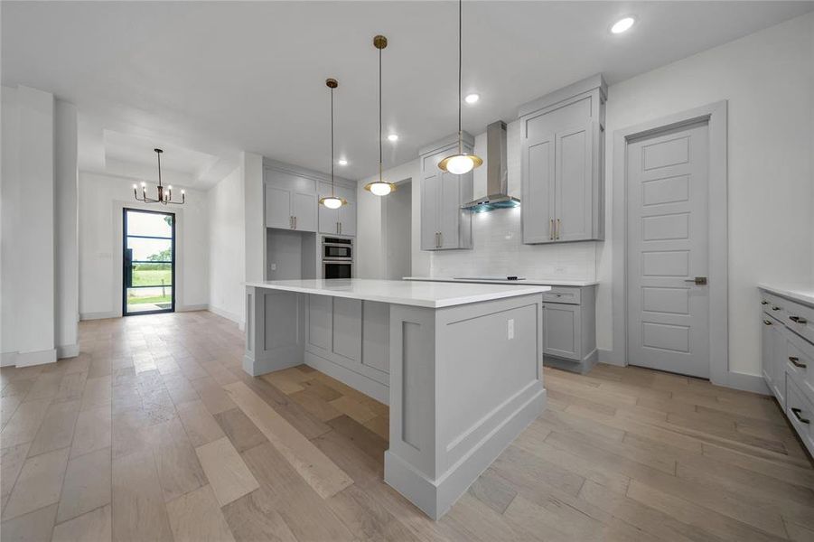 Kitchen with wall chimney range hood, backsplash, gray cabinets, and light hardwood / wood-style floors