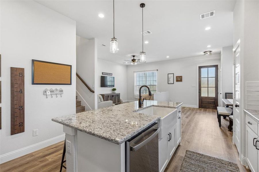 Kitchen with a center island with sink, stainless steel dishwasher, wood-type flooring, decorative light fixtures, and a kitchen bar