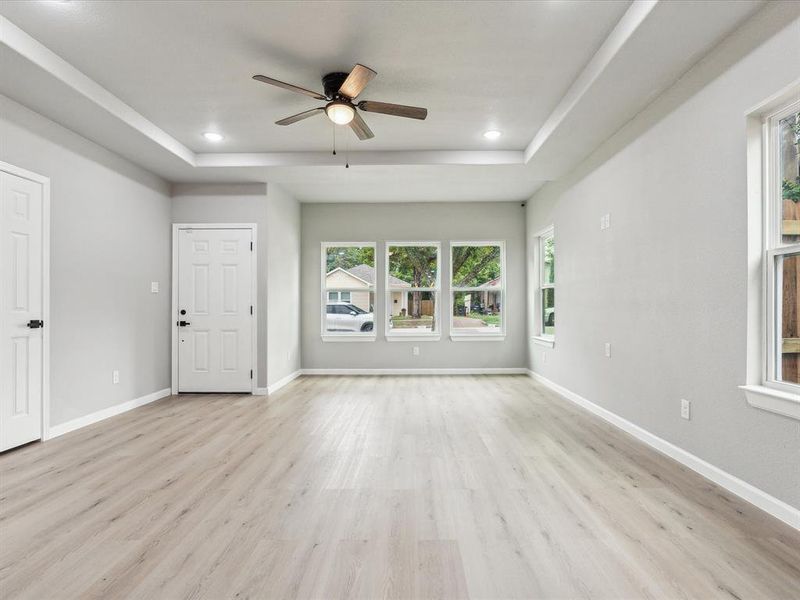 Empty room with ceiling fan, light wood-type flooring, and a tray ceiling