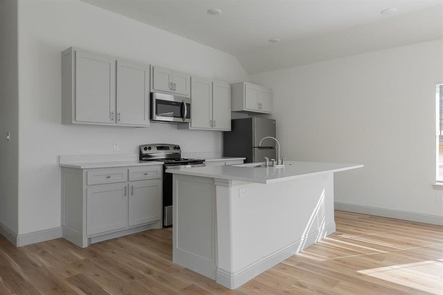 Kitchen with appliances with stainless steel finishes, an island with sink, gray cabinets, lofted ceiling, and light hardwood / wood-style flooring