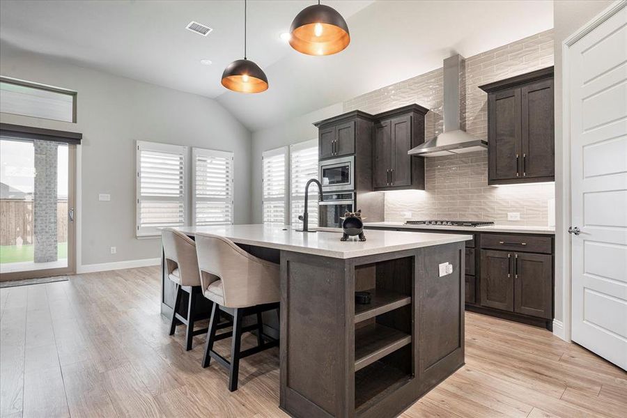 Kitchen featuring stainless steel appliances, decorative backsplash, light wood-type flooring, wall chimney exhaust hood, and a center island with sink