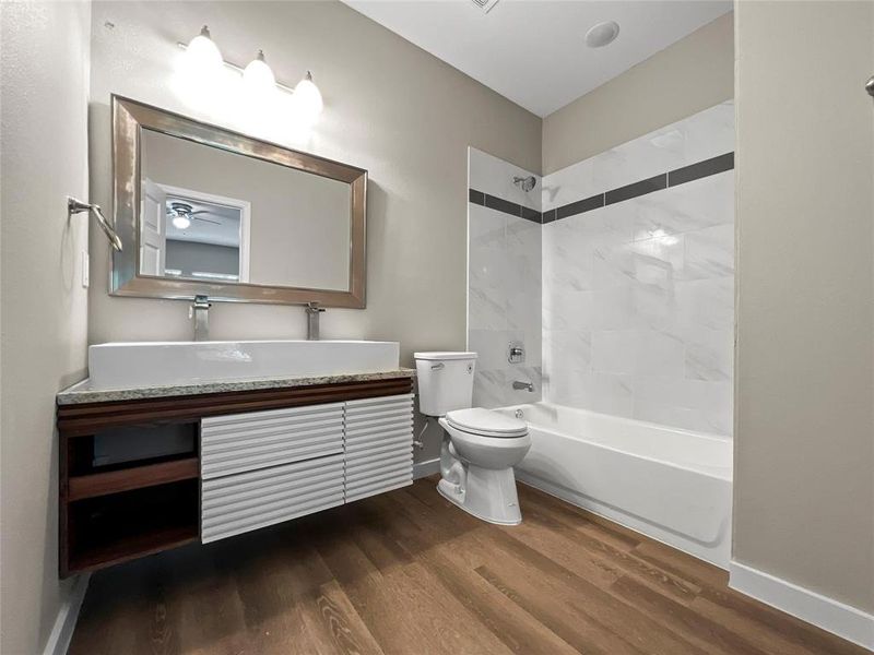 Full bathroom with vanity with extensive cabinet space, hardwood / wood-style floors, toilet, and tiled shower / bath combo