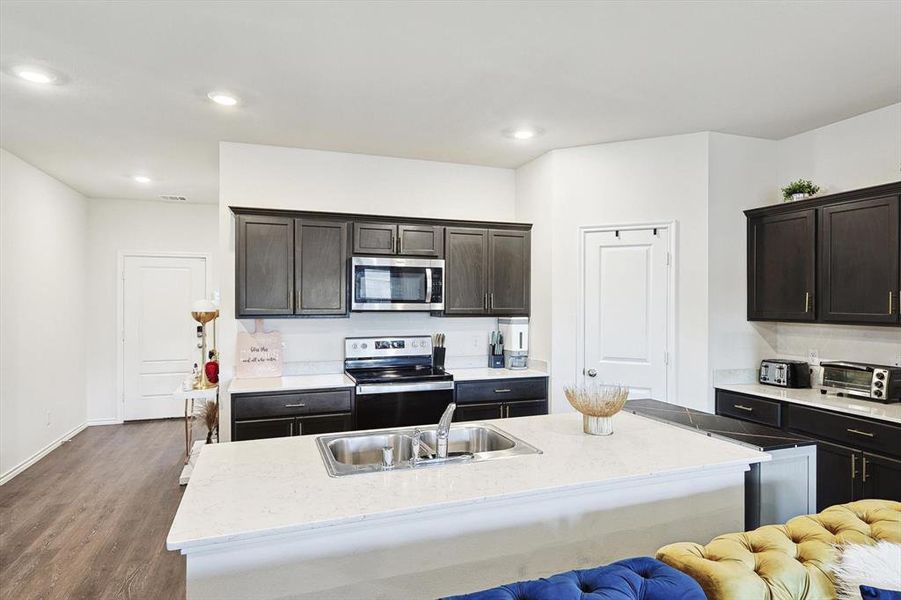 Kitchen with dark brown cabinets, appliances with stainless steel finishes, dark hardwood / wood-style floors, and a kitchen island with sink