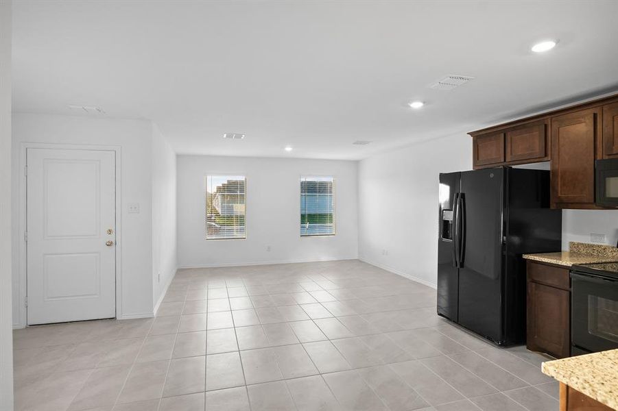 Kitchen with light stone countertops, dark brown cabinets, black appliances, and light tile patterned floors