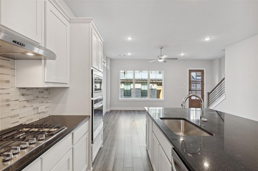 Kitchen with stainless steel appliances, wood-type flooring, backsplash, sink, and white cabinetry