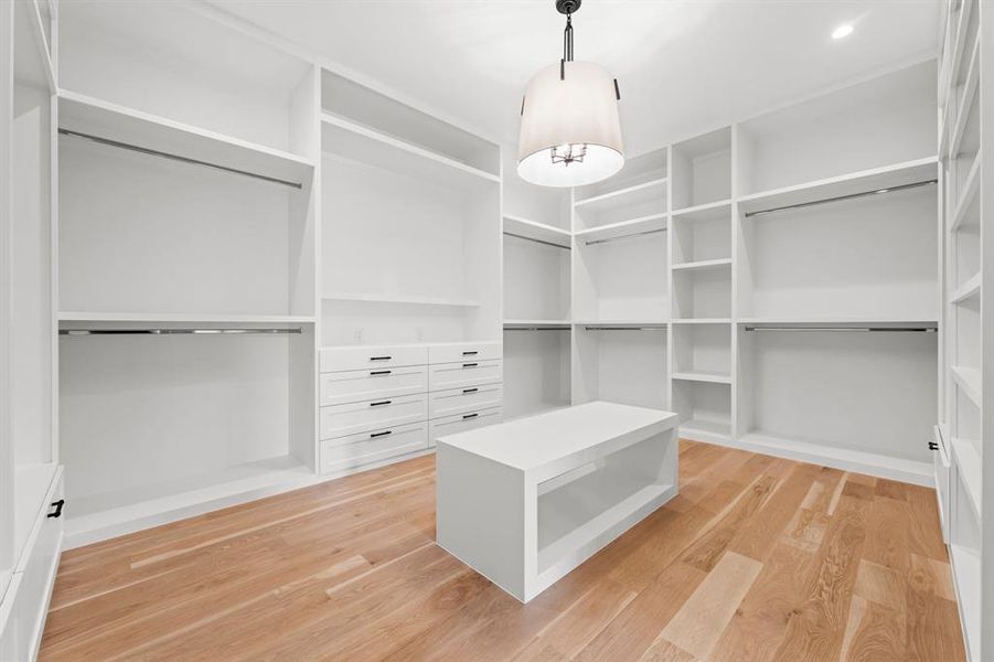 The primary closet features numerous chests of drawers, long and standard hanging space, bag and shoe storage, as well as bench space and a chandelier.