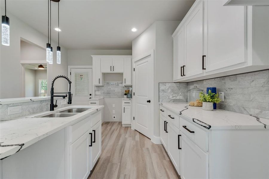 Kitchen with light wood-type flooring, light stone counters, decorative backsplash, pendant lighting, and sink