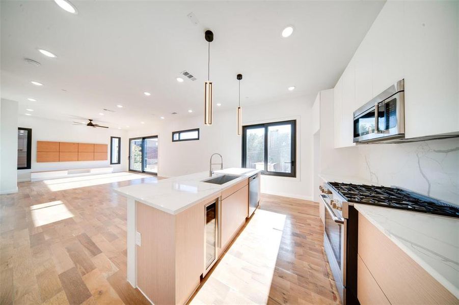 Kitchen with a kitchen island with sink, light hardwood / wood-style flooring, sink, pendant lighting, and stainless steel appliances