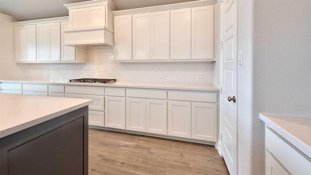 Kitchen with premium range hood, decorative backsplash, white cabinets, stainless steel gas stovetop, and light hardwood / wood-style floors