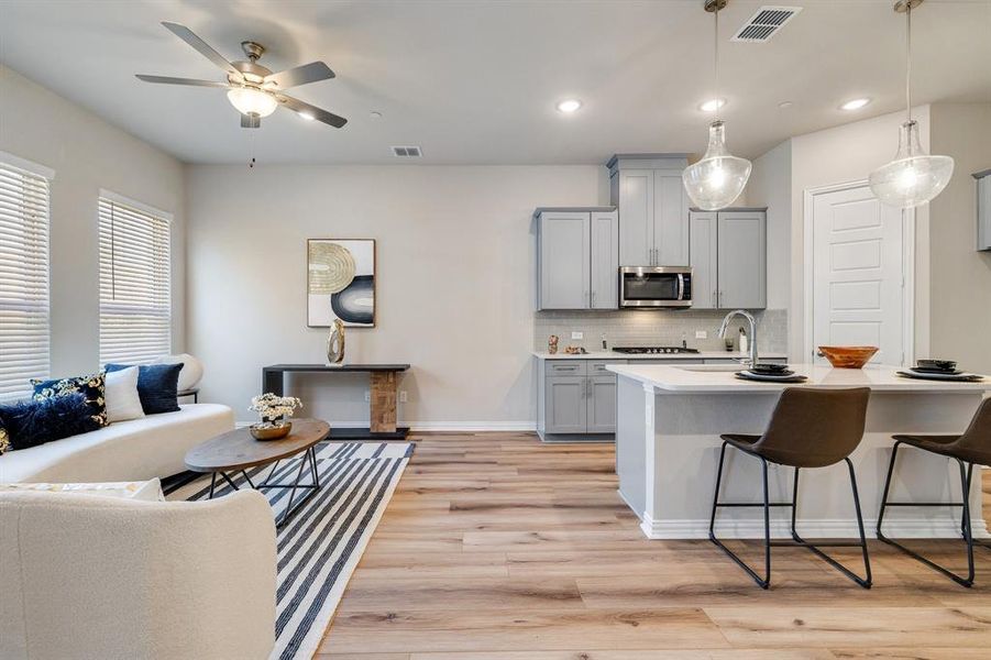 Kitchen with gray cabinets, pendant lighting, light hardwood / wood-style floors, an island with sink, and ceiling fan