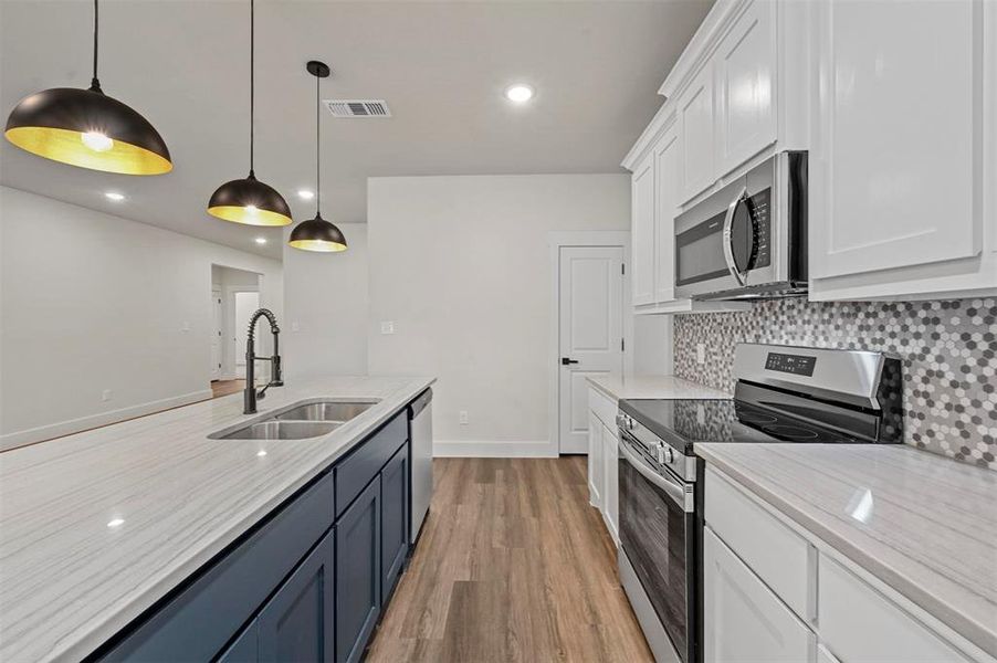 Kitchen with appliances with stainless steel finishes, hanging light fixtures, white cabinetry, light wood-type flooring, and sink