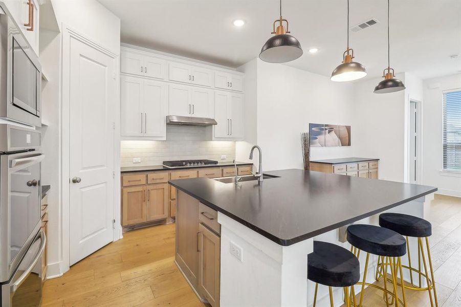 Kitchen with white cabinetry, light hardwood / wood-style flooring, an island with sink, backsplash, and sink