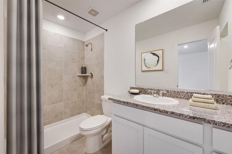 Bathroom with tile floors, curtained shower, toilet, and vanity with extensive cabinet space