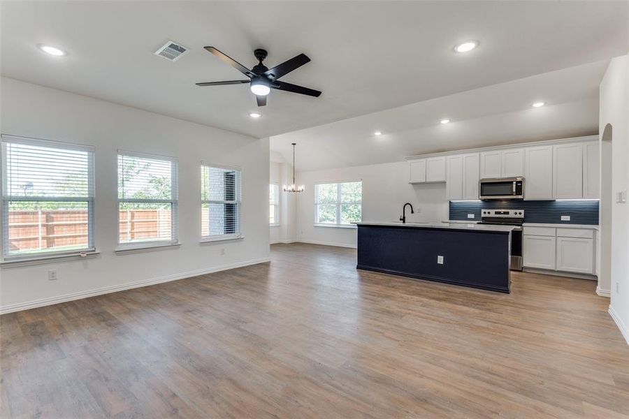 Kitchen with pendant lighting, light hardwood / wood-style floors, a kitchen island with sink, white cabinets, and appliances with stainless steel finishes