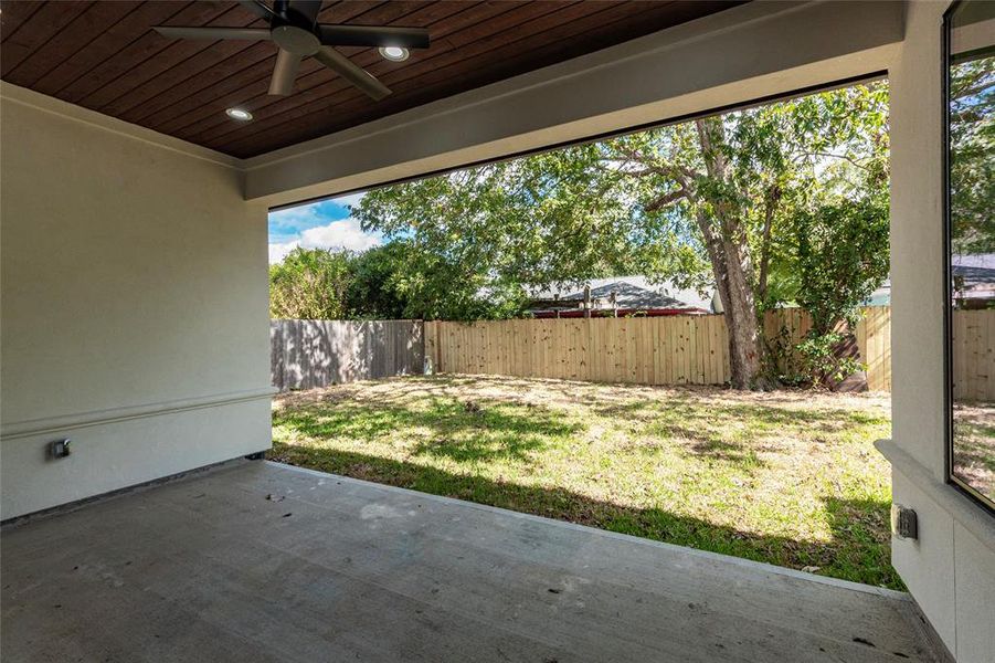 The covered patio has a wood planked ceiling with recess lighting and an outside fan.