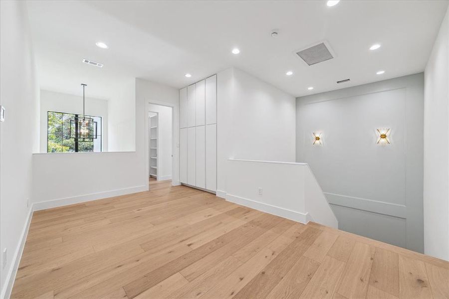 Ascend to the second floor, where dual designer brass sconces complement a Sherwin Williams Sea Salt accent wall in the stairwell. At the top of the stairs, concealed storage cabinets provide discreet and convenient storage solutions.