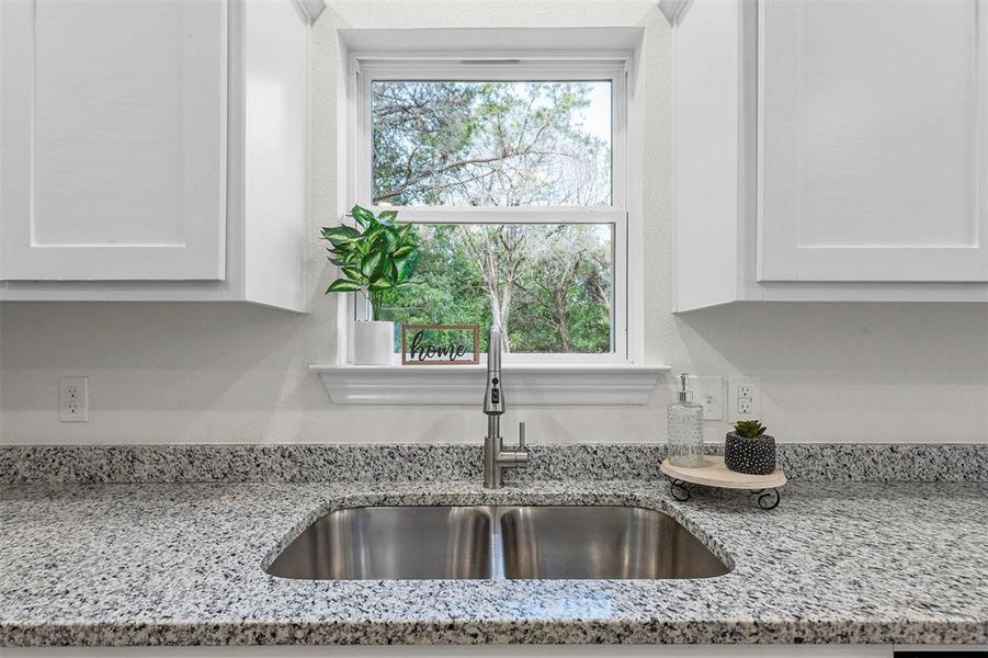 Room details featuring sink, white cabinetry, and light stone countertops