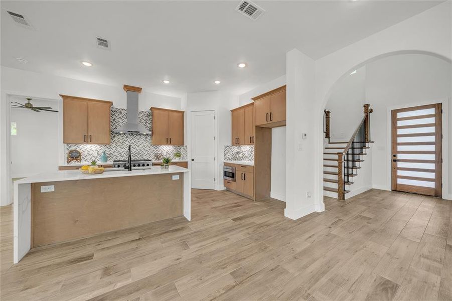 Kitchen featuring tasteful backsplash, light wood-type flooring, ceiling fan, and wall chimney range hood
