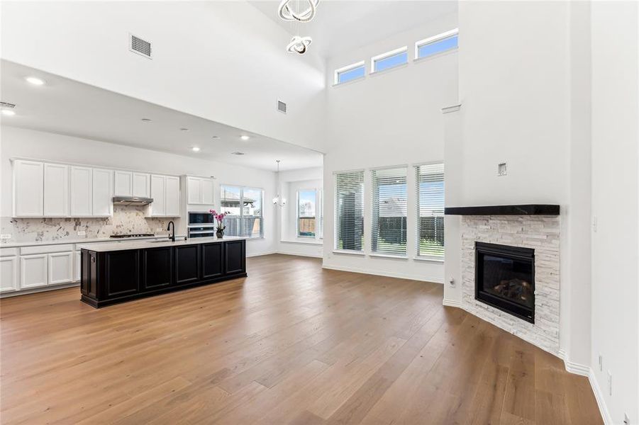 Kitchen with light hardwood / wood-style floors, white cabinets, a fireplace, a high ceiling, and a kitchen island with sink