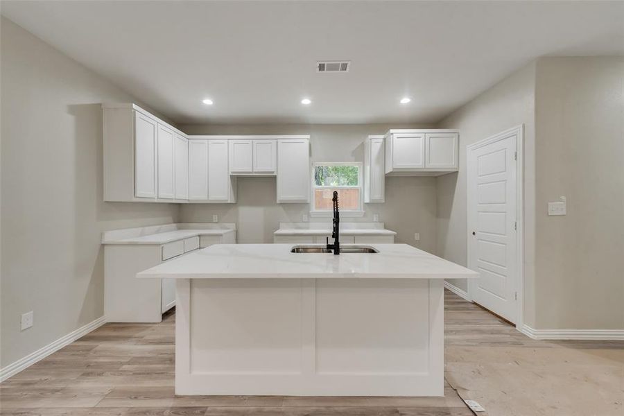 Kitchen featuring sink, light stone counters, a kitchen island with sink, light wood-type flooring, and white cabinetry