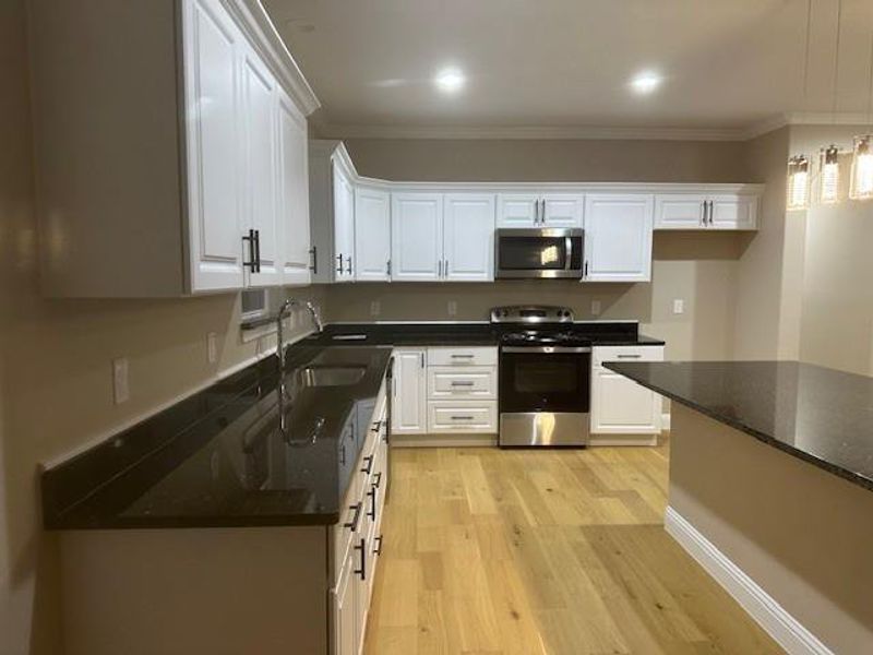 Kitchen with white cabinets, appliances with stainless steel finishes, ornamental molding, and light hardwood / wood-style flooring