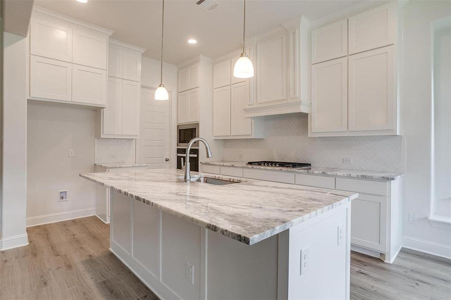 Kitchen with backsplash, light hardwood / wood-style flooring, a kitchen island with sink, and sink