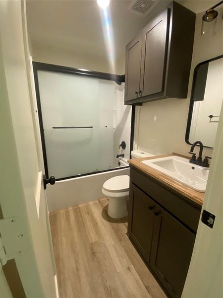 Hall bathroom shower combo with glass door, vanity, hardwood / wood-style floors, and toilet