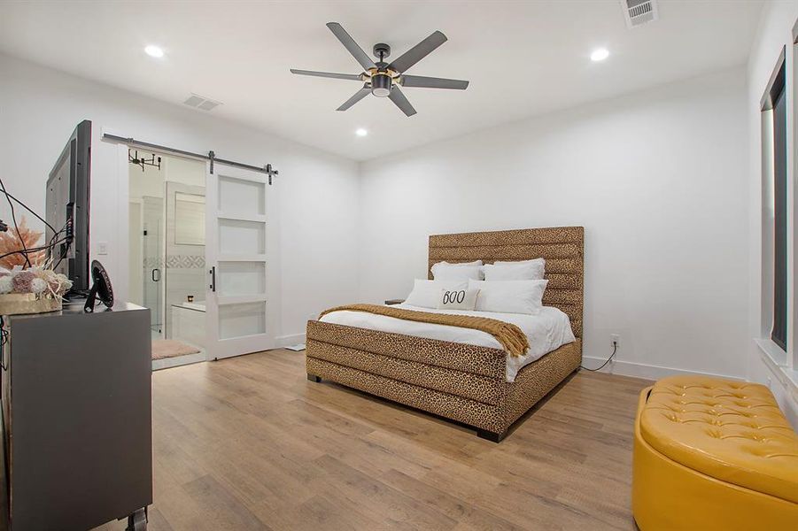 Bedroom with ceiling fan, light wood-type flooring, and a barn door