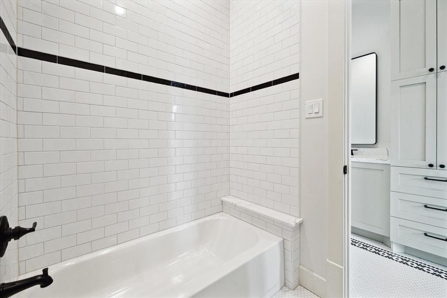 Bathtub in the shared secondary bath with white subway tile in a traditional brick pattern accented by a black accent tile for some contrast that compliments the black plumbing fixtures and hardware.