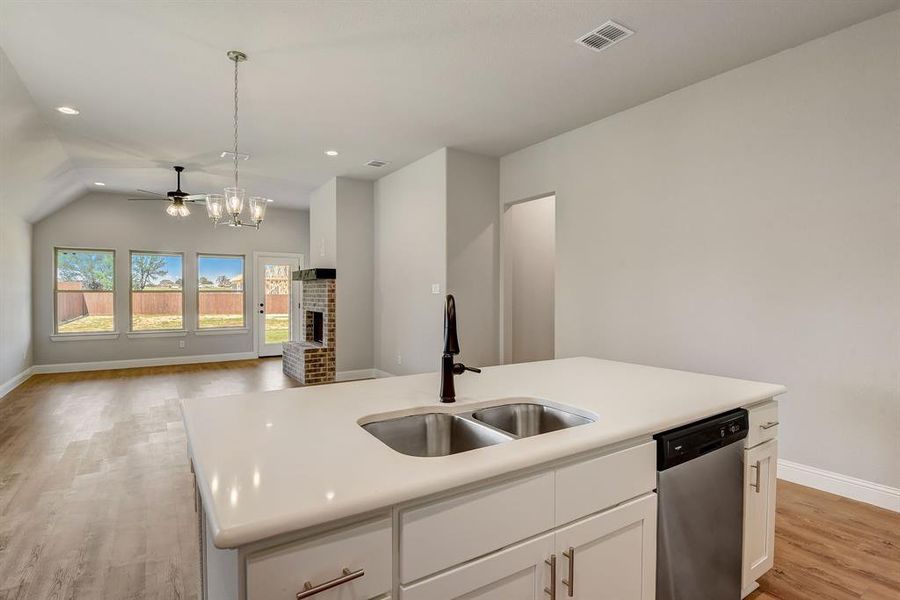 Kitchen with light hardwood / wood-style floors, a kitchen island with sink, a brick fireplace, pendant lighting, and dishwasher