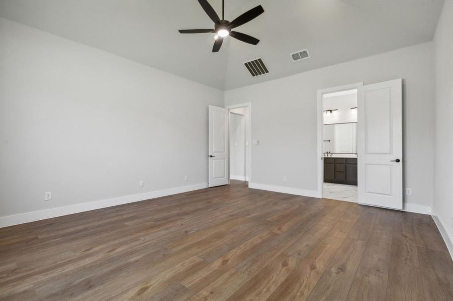 Unfurnished bedroom with vaulted ceiling, hardwood / wood-style floors, connected bathroom, and ceiling fan