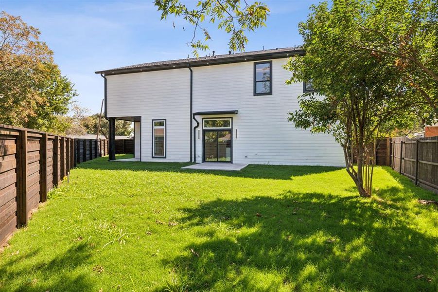 Back of house featuring a grassed yard, some trees and wood fence