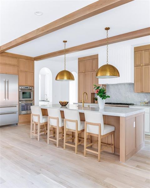 Kitchen featuring appliances with stainless steel finishes, light hardwood / wood-style flooring, pendant lighting, and an island with sink