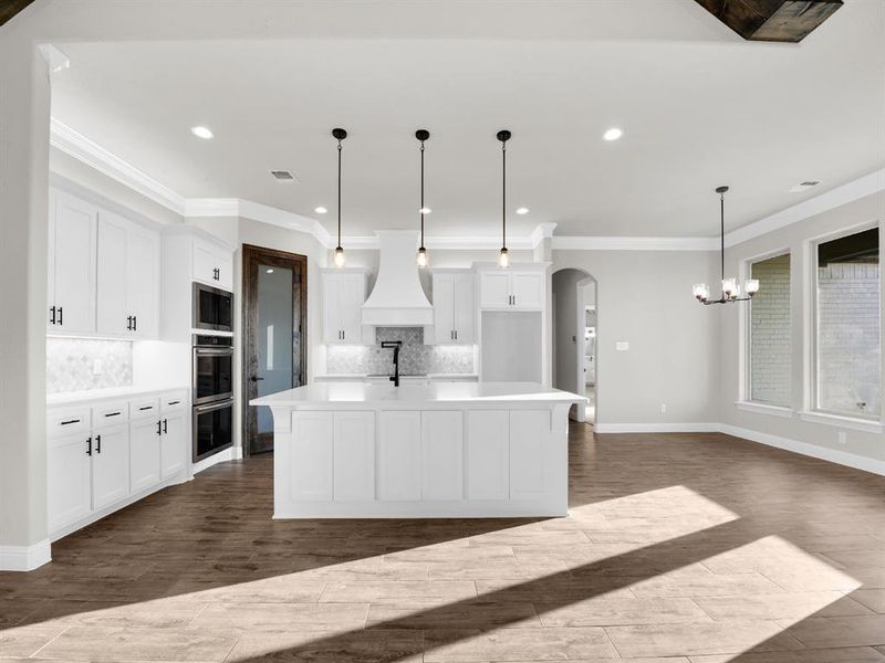 Kitchen with tasteful backsplash, stainless steel appliances, a center island with sink, decorative light fixtures, and premium range hood