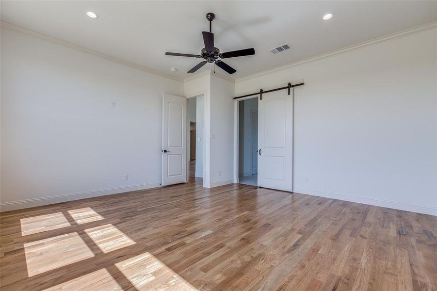 Unfurnished bedroom with a barn door, crown molding, light wood-type flooring, and ceiling fan